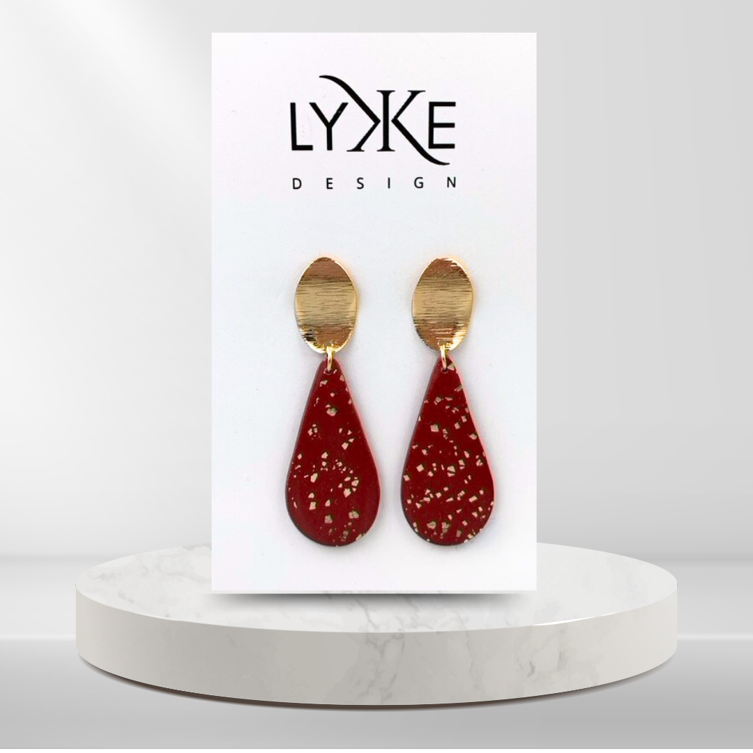 Gullfargede øredobber med stor rød dråpe med gullblad-effekt